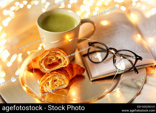 croissants, matcha tea, book and glasses in bed