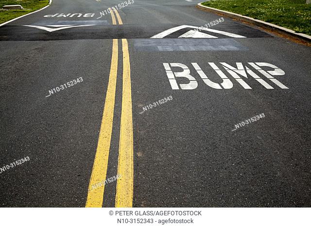 Street with double yellow lines, speed bumps, and the word ""Bump"" painted on it