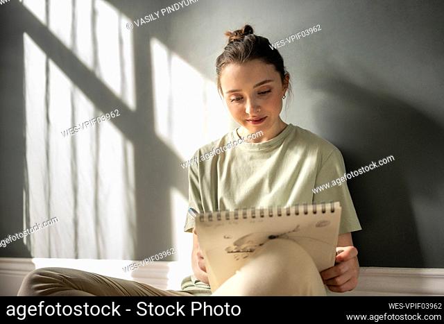Young woman drawing on note pad while leaning on wall