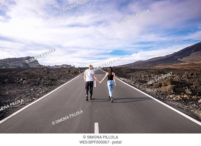 Spain, Tenerife, back view of couple walking hand in hand on empty road at Teide National Park