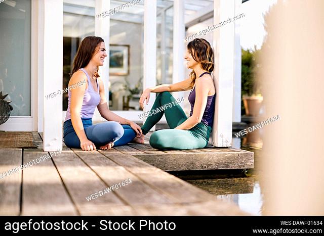 Female friends talking while sitting by columns on hardwood floor