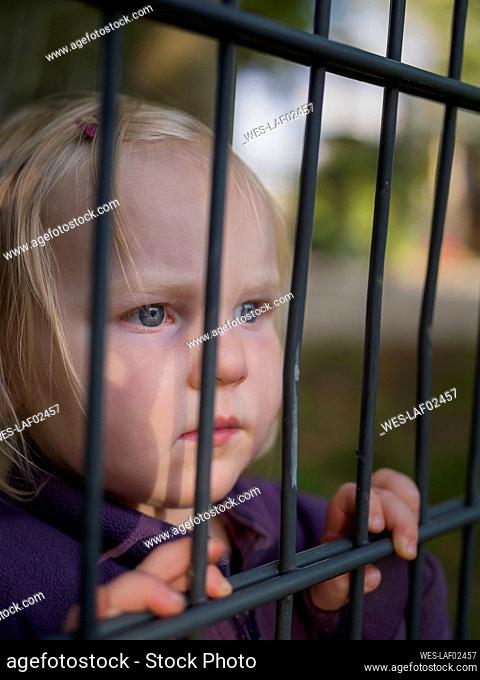 Portrait of serious toddler girl behind fence looking at distance