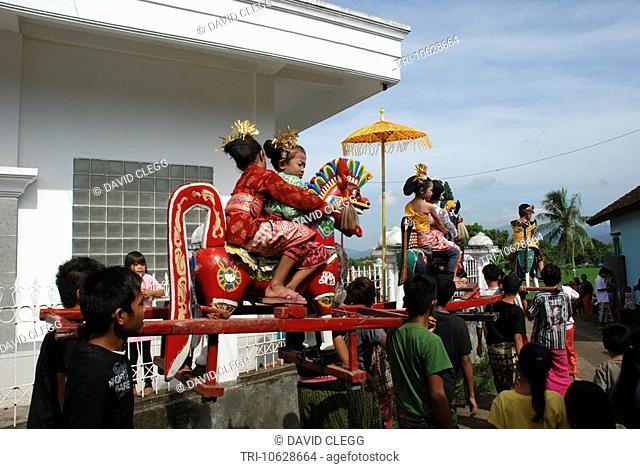 Muslim boys and girls aged 6 years in traditional dress are carried aloft outside mosque on ornately carved and painted wooden horses in circumcision rites