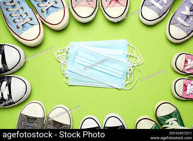 many multi-colored textile well-worn sneakers of different sizes and a stack of medical disposable masks on a green background
