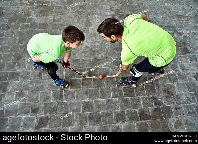 Boy in face off with father while playing roller hockey on court