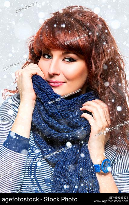 Young beautiful woman with knitted blue wool scarf wrapped around her neck. Snow flakes on the background