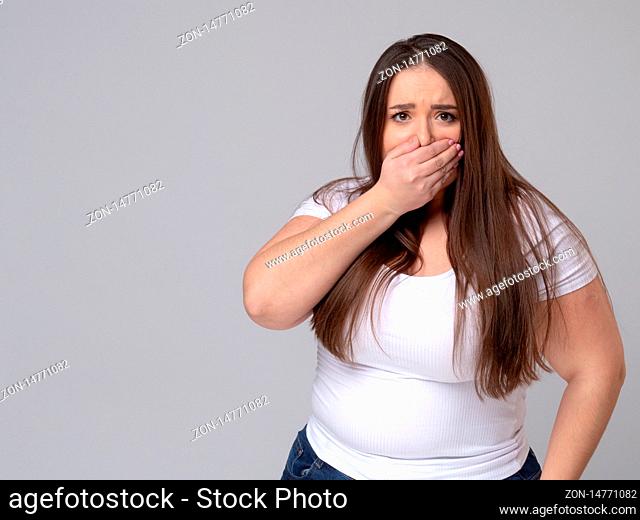 Frightened plus size girl closes her mouth with her hand so as not to scream