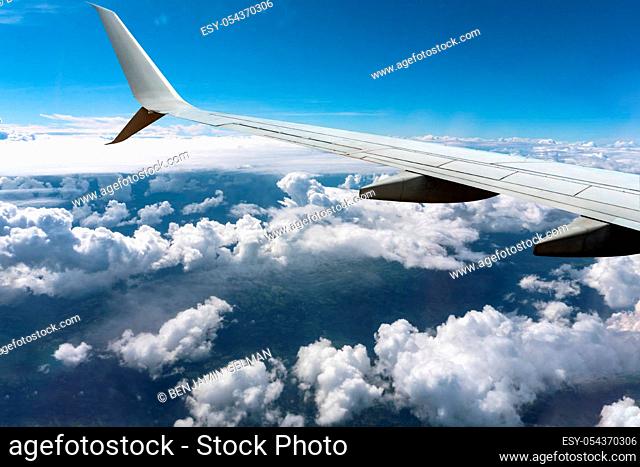 White clouds float under the wing of a sunlit airplane flying under a blue sky.