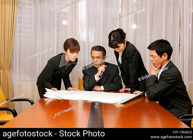Business people reviewing blueprints in office conference room