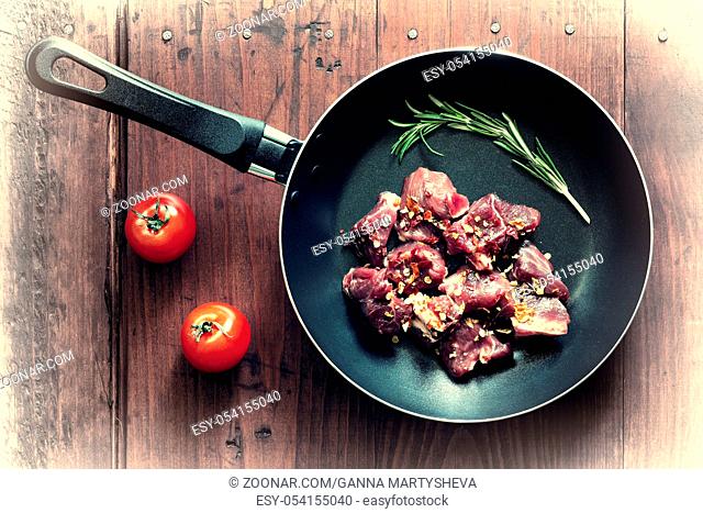 Raw goulash beef in a frying pan with rosemary and spices. Concept: home cooking
