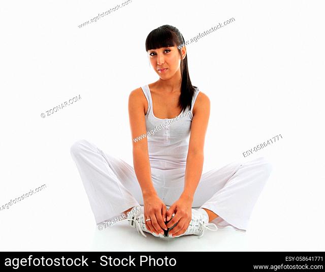 A young woman wearing fitness sportswear. She is doing a groin and inner thigh stretch sitting on the floor with feet together and using effort to push knees to...