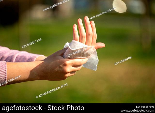 Cleaning hands with wet wipes outdoor against disease infection versus flu or infulenza, blurred green background