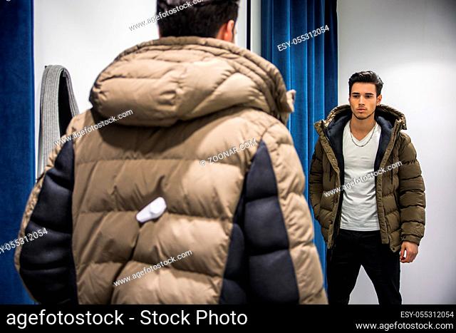 Young Handsome Man Trying on Clothes in Clothing Store#39;s Changing Room in Front of a Mirror or in Room Closet