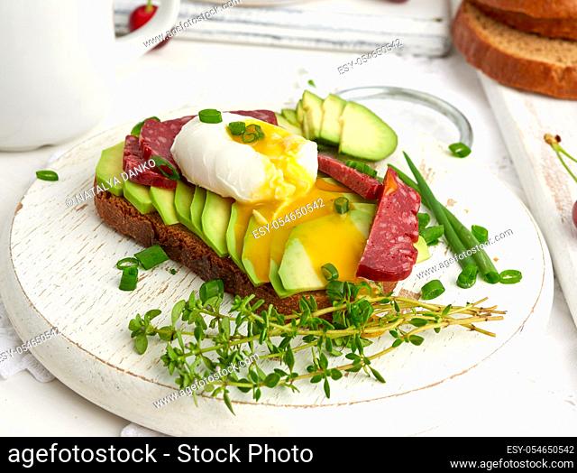 toast with poached egg and avocado on a round board, morning breakfast, top view on a white table