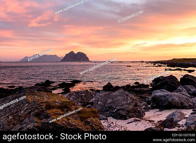 Scenic cloudscape with sunrise over the Lofoten islands in Norway in summer. . View from Vaeroy. Rocks and beach in the foreground The island Mosken in the...