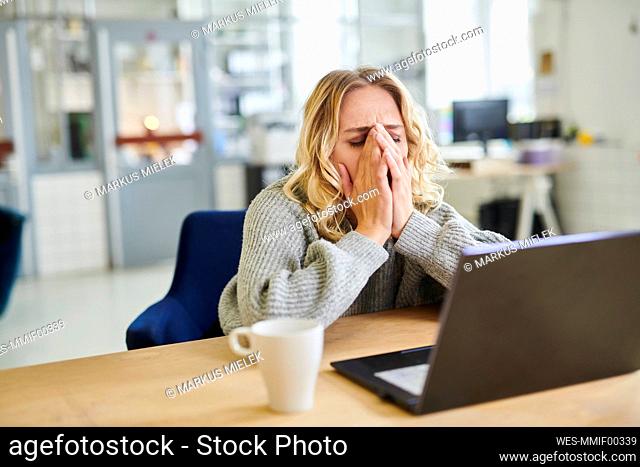 Frustrated young woman sitting at desk in office with laptop