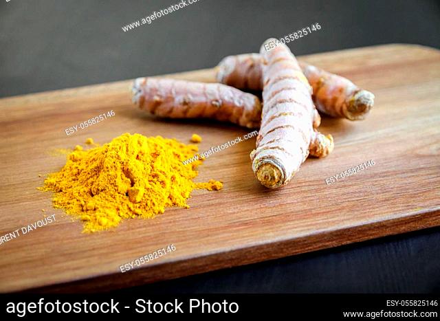 Turmeric root and spice powder on a wooden cutting board