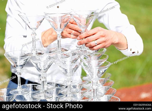 Waiter builds a pyramid of glasses for champagne at outdoor garden in wedding ceremony