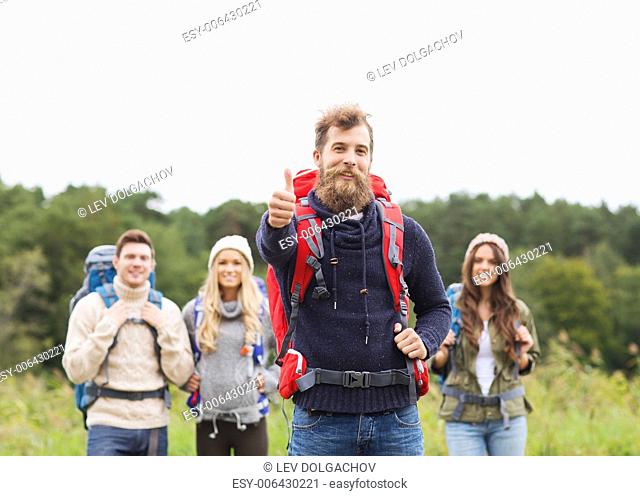 travel, tourism, hike, gesture and people concept - group of smiling friends with backpacks standing and showing thumbs up outdoors