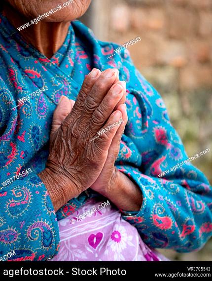 Unrecognized elder nepalise woman wearing blue cloths crossing her wrinkled hands