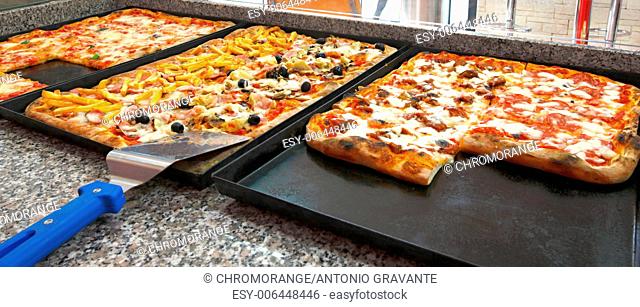 Counter of the pizzeria with trays and square pieces of pizza