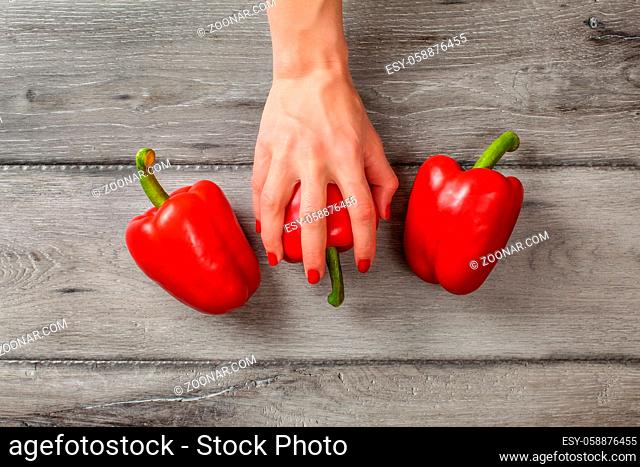 Table top view - gray wood desk and woman hands placed on red bell pepper, with two more at each side