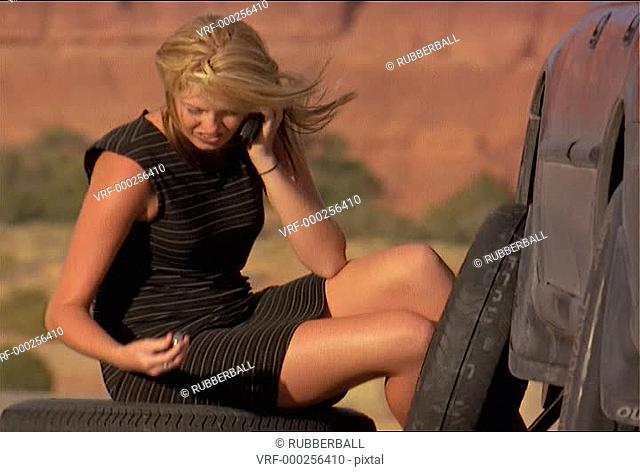 medium shot of an attractive blonde woman as she calls for help with her cell phone while being stuck in the middle of nowhere