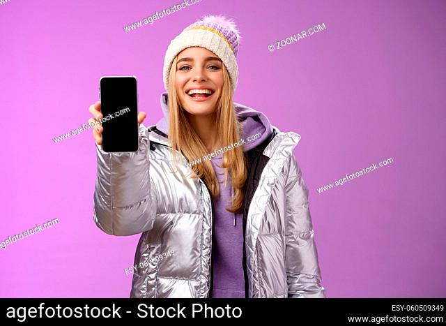 Sassy delighted cheerful blond woman recommend use app edit perfect pictures holding smartphone showing mobile phone display proudly satisfactory smile camera