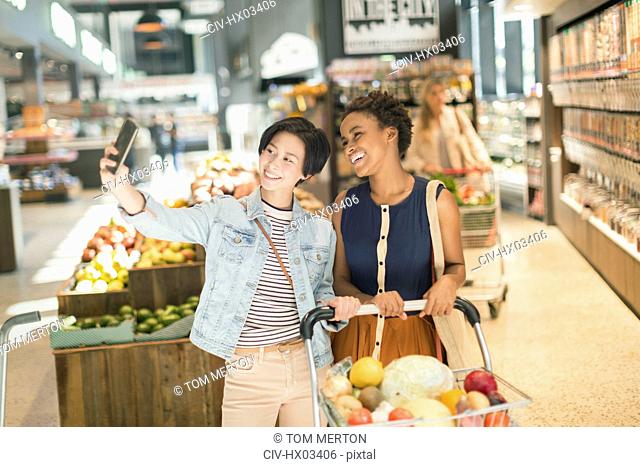 Smiling young lesbian couple taking selfie in grocery store market