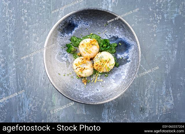 Modern style fried scallops with crumbles and lemon slices served with kalette cilanto relish as top view on a Nordic design plate with copy space