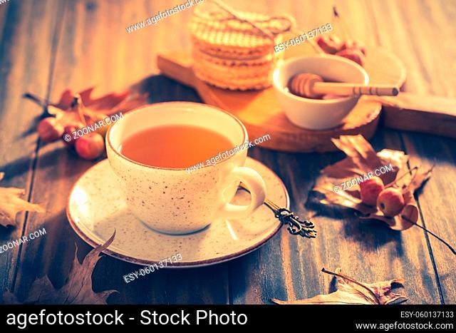 Hot tea with honey, homemade wafer biscuit and autumn leaves on wooden background