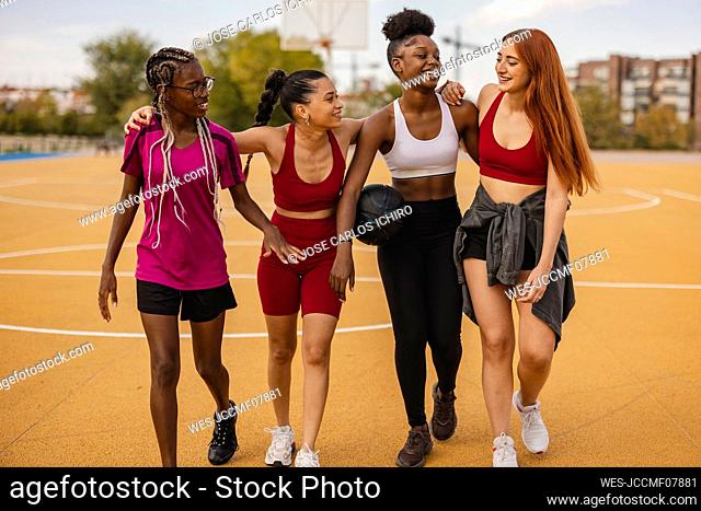 Happy young friends walking together in basketball court