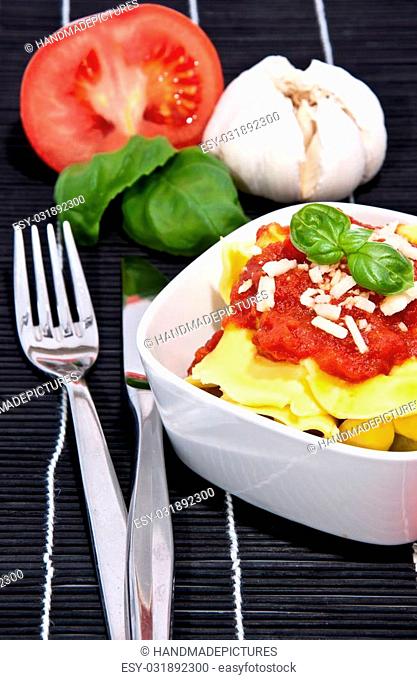 Tortellini with blurred ingredients in the background on a black tablecloth