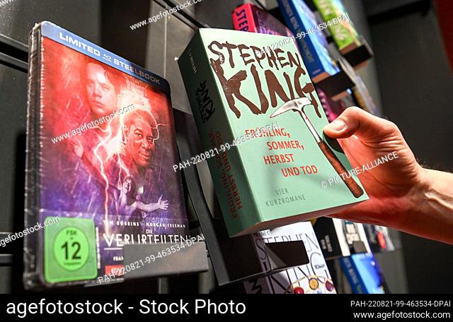 PRODUCTION - 11 August 2022, Berlin: ILLUSTRATION - A man reaches for Stephen King's book ""Spring, Summer, Autumn and Death"" in the Dussmann department store