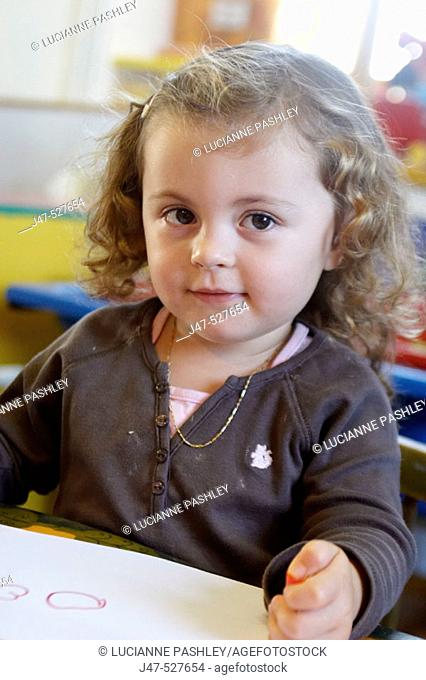 3 year old girl sitting at nursery drawing, smiling off camera