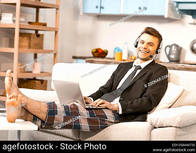 Positive Entrepreneur Works At Home, Happy Freelancer In Headphones Enjoys Conversation With Clients Sitting On Kitchen Sofa