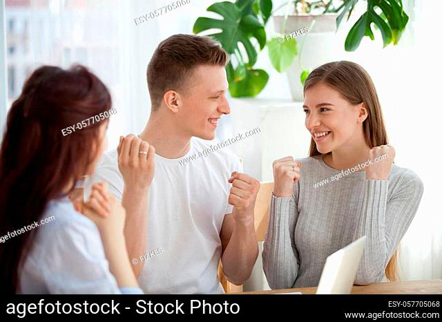 Excited millennial couple gesture yes happy signing contract with real estate agent, smiling first time buyers feel euphoric closing deal with broker