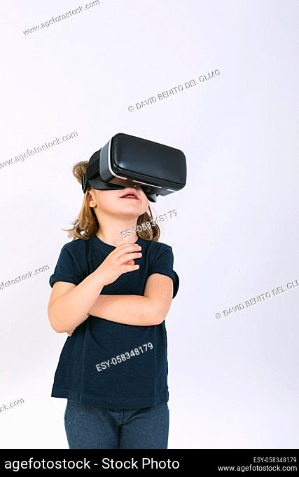 Little girl with virtual reality glasses looking up on white background