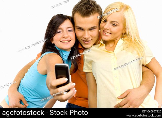 Two young woman and a man between them. They're making a photo by mobile phone. Isolated on white in studio