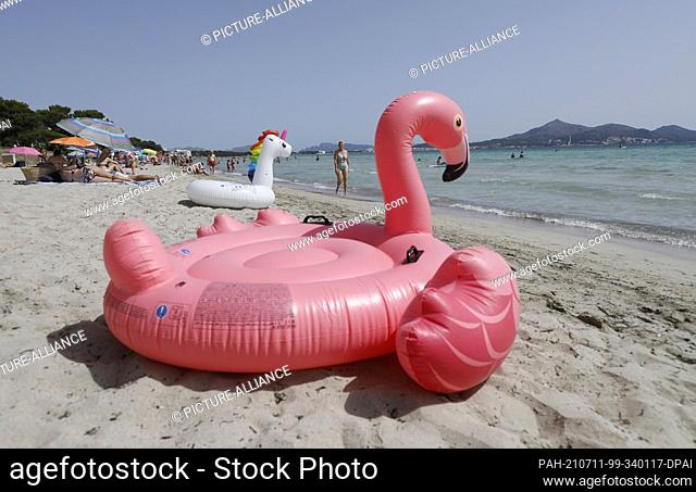 11 July 2021, Spain, -: An inflatable pink flamingo lies on the beach of Playa de Muro in the north of Mallorca. The federal government has declared all of...