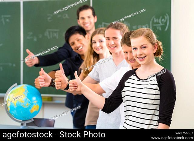 School class teacher and students stand in front of a blackboard with math work in a classroom during lesson