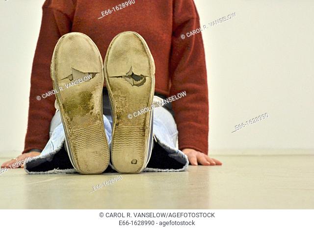 woman sitting on floor, wearing worn out sneakers