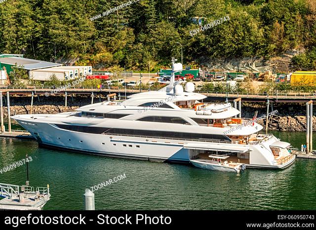 September 14, 2018 - Juneau, Alaska: Sleek white luxury yacht docked in city harbor amongst industrial surroundings