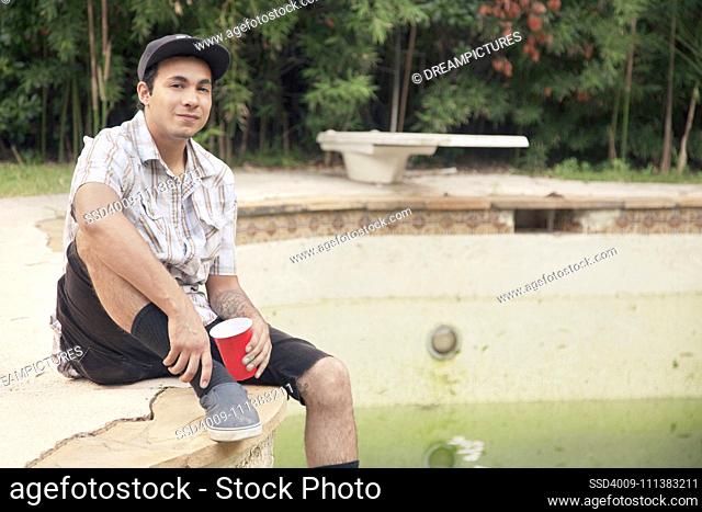 Mixed race man sitting on edge of disused swimming pool