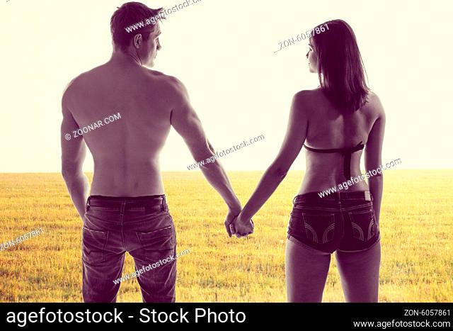 Atmospheric conceptual image of the silhouettes of a romantic young couple holding hands standing with their backs to the camera in a field