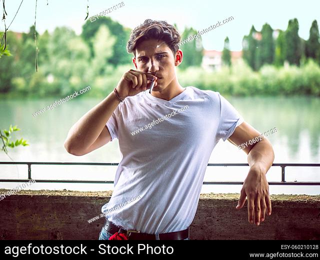 Handsome stylish young man smoking outside in urban setting, looking at camera