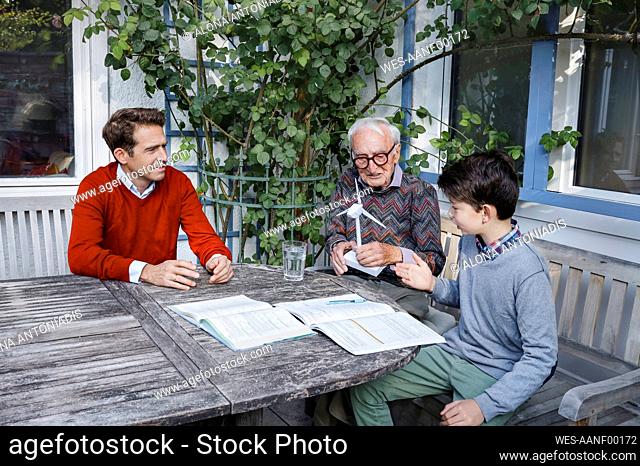 Boy explaining to grandfather and father in backyard