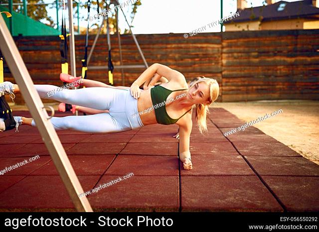 Women's group doing abs exercise with ropes on sports ground, front view, outdoors fitness training. Slim female athletes in sportswear, team fit workout