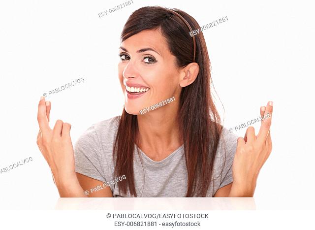 Headshot portrait of attractive lady crossing her fingers while smiling and looking at camera on isolated studio