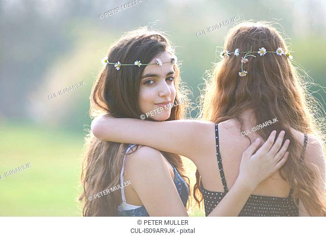 Rear view portrait of two teenage girls wearing daisy chain headdresses in park